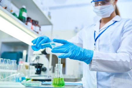 戴防护手套的女科学家肖像在医学实验室研究化学药品时, 将有色液体